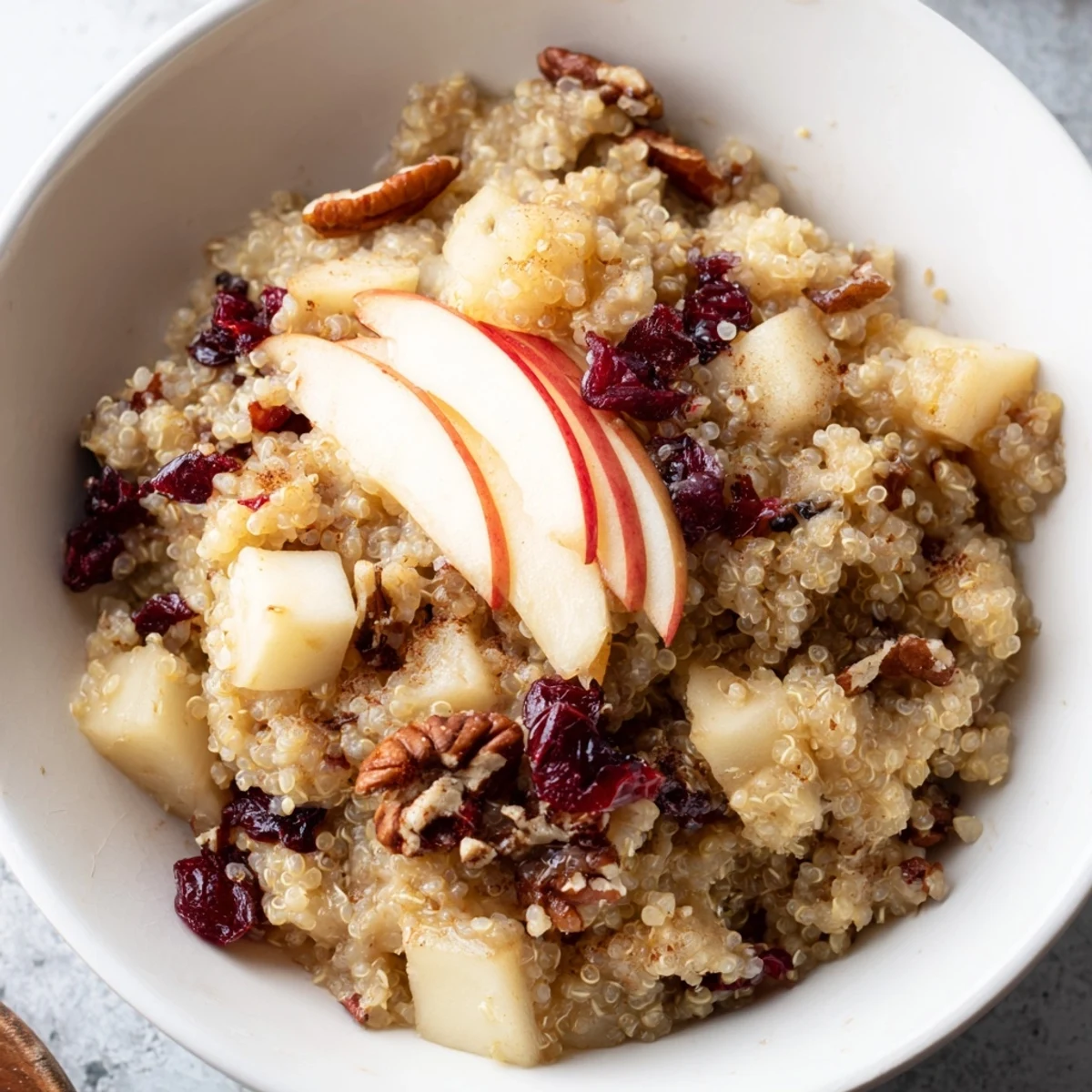 Steaming Apple Cinnamon Quinoa Bowl, topped with nuts and fruit, a cozy and nutritious breakfast.