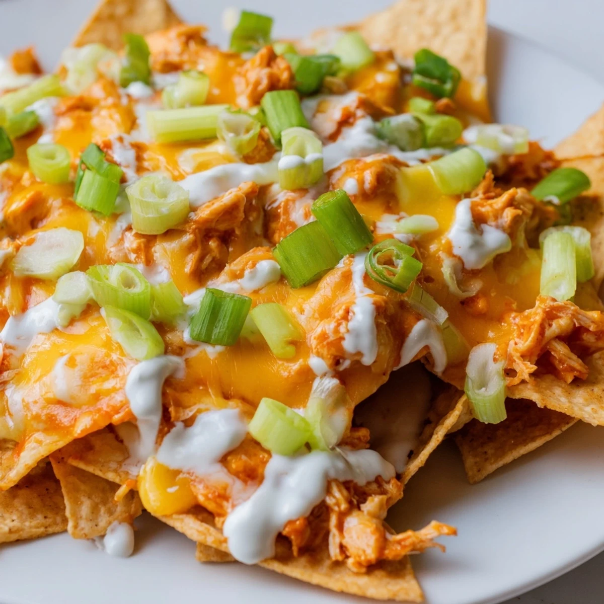 A close-up view of Buffalo Chicken Nachos with melted cheddar and Monterey Jack cheese bubbling over crispy tortilla chips and spicy shredded chicken.  