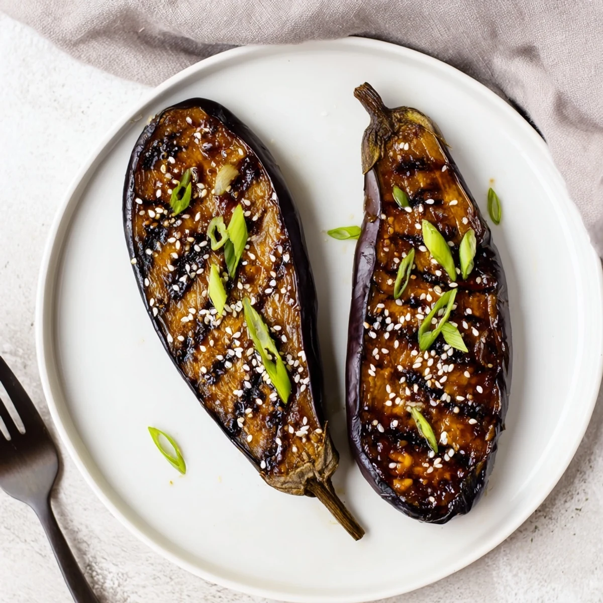 Golden-brown miso glazed eggplant halves on a baking sheet, garnished with toasted sesame seeds and fresh green onions.