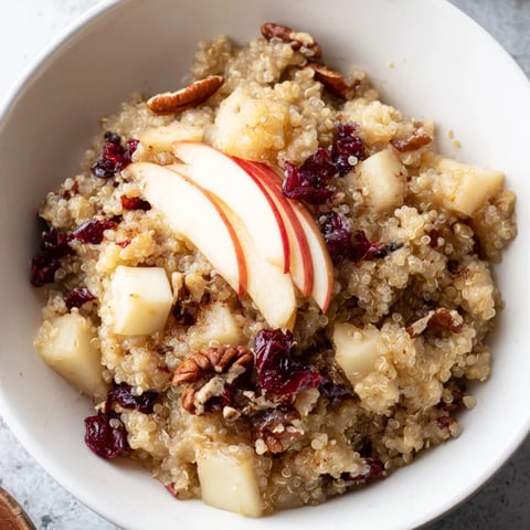 Steaming Apple Cinnamon Quinoa Bowl, topped with nuts and fruit, a cozy and nutritious breakfast.