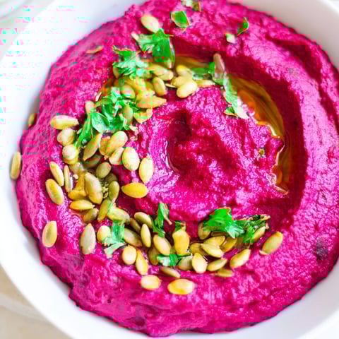 Vibrant beet hummus swirled with olive oil, ready to scoop with warm pita bread.