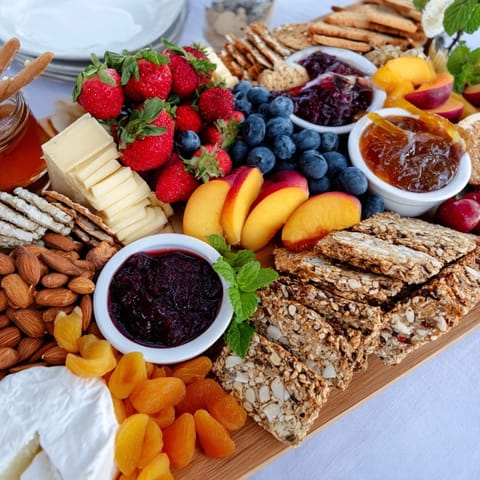Beautifully arranged jam-infused brunch board features vibrant fresh fruits and crispy breads.  