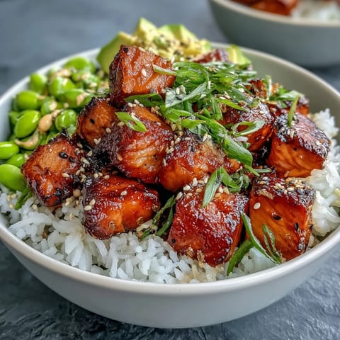 A close-up of a Salmon Rice Bowl, drizzled with spicy sriracha mayo and sprinkled with sesame seeds.