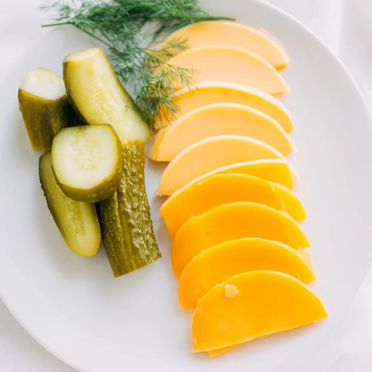 Fresh dill sprigs alongside sharp cheddar and tangy dill pickles making a colorful, gluten-free snack.